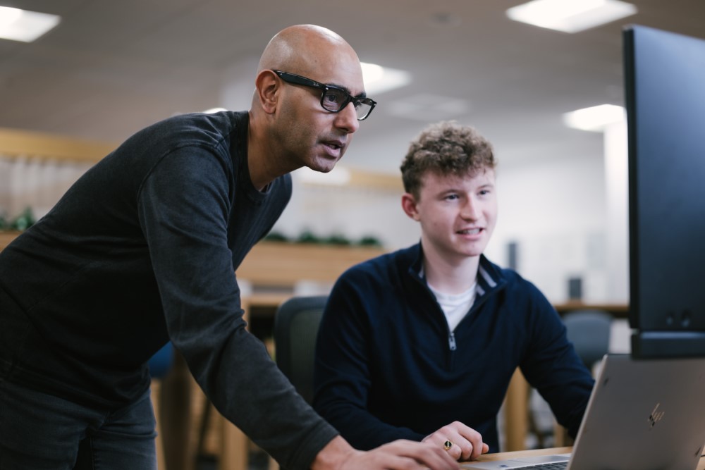 Amjad helping a colleague, both of them looking at a computer screen