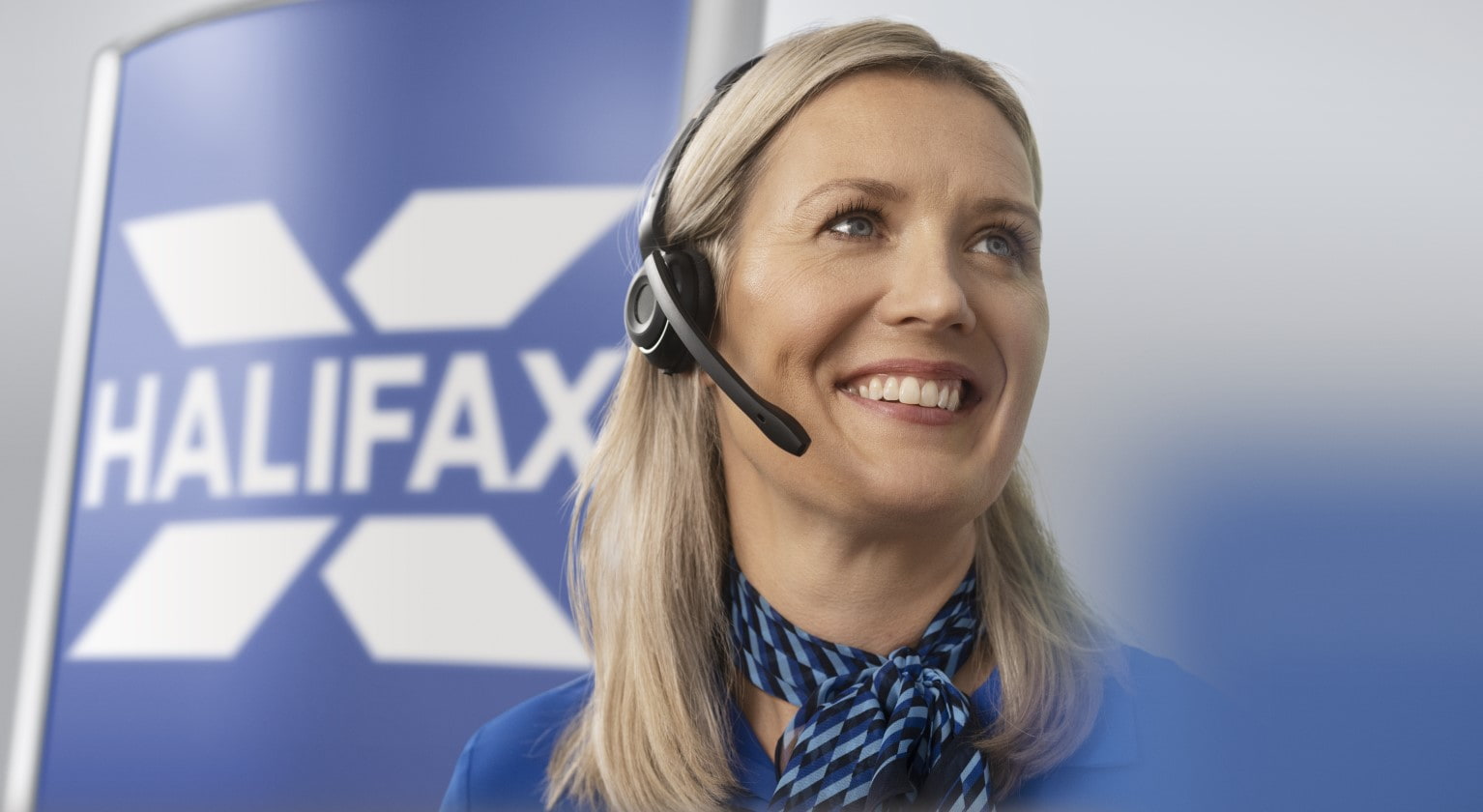 Kate smiling and talking on a headset in front of a Halifax logo sign