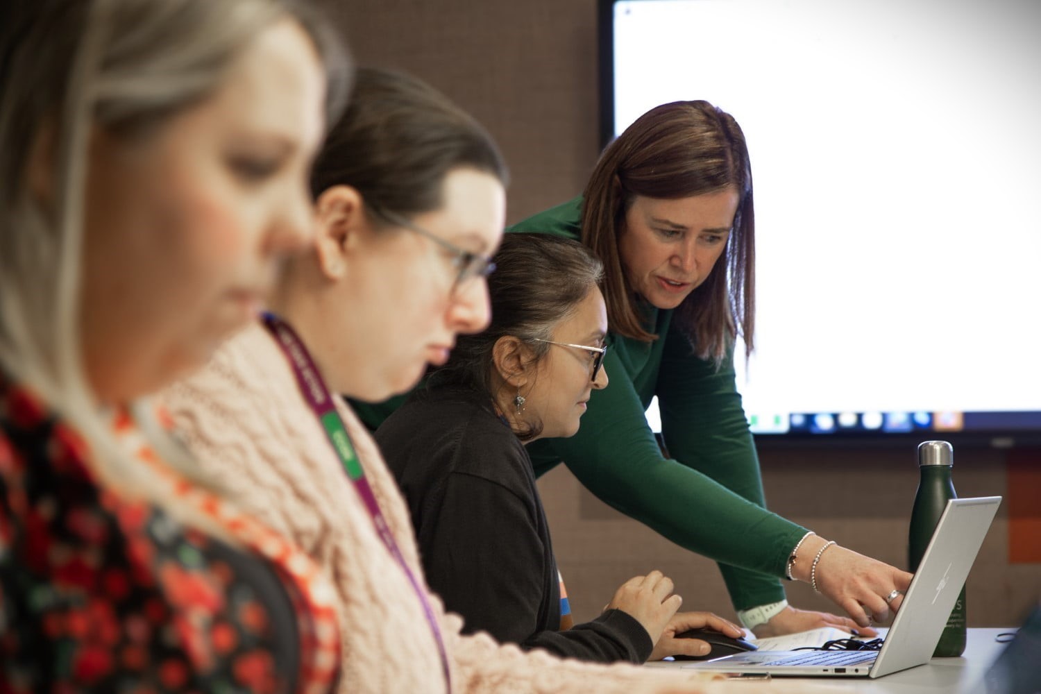 Lisa teaching a group of colleagues, talking and pointing to someone's laptop screen