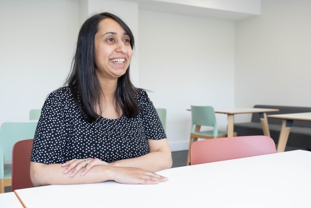 Amreen sitting at a table in the office smiling at something off-camera.