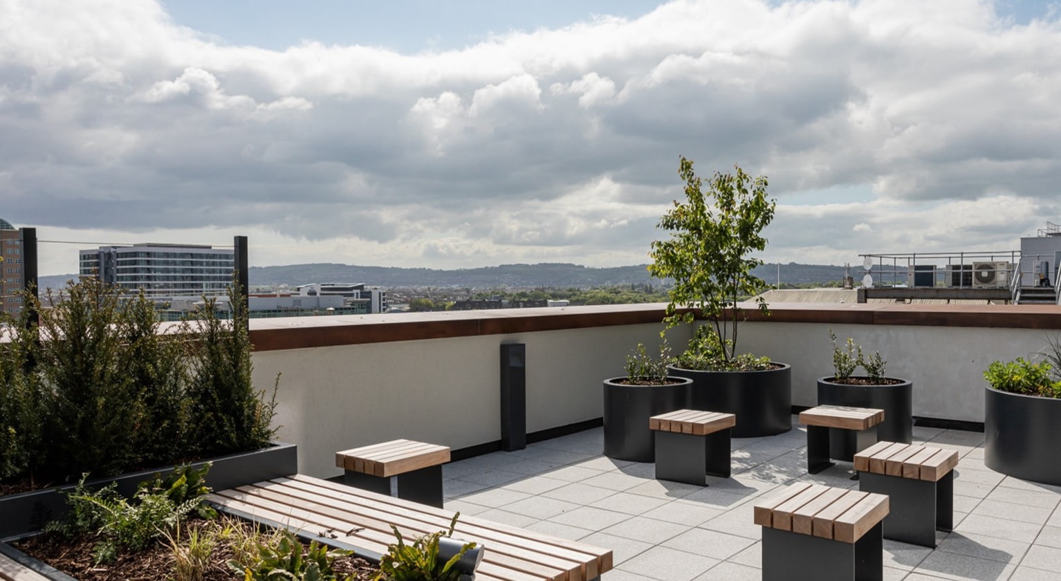 Roof terrace in The Paper Exchange building in Belfast, with modern seating, greenery and a view of the city. 