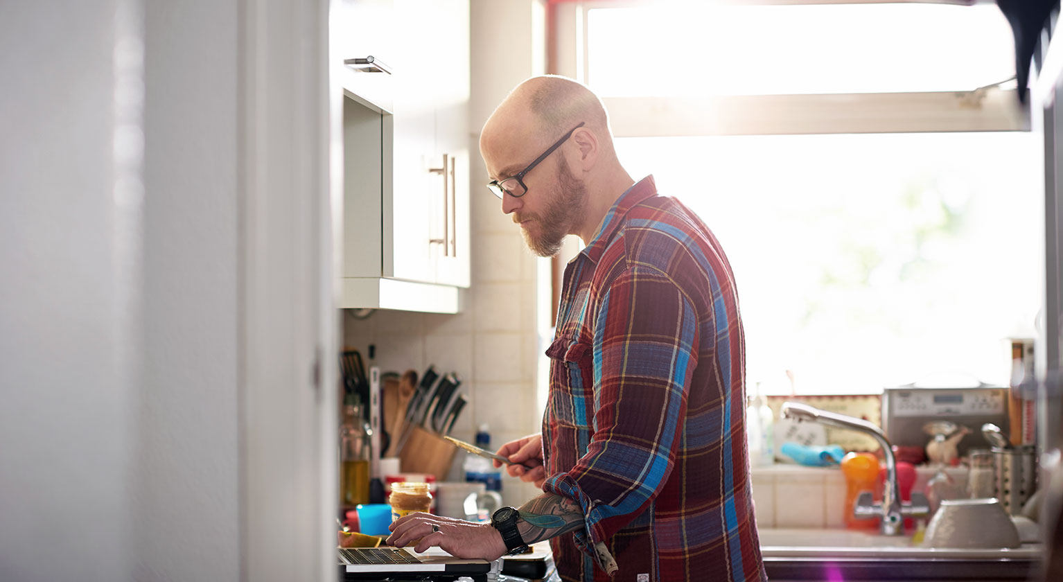 Man in kitchen checking laptop computer