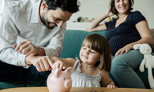 Man, woman and child putting money in a piggy bank 