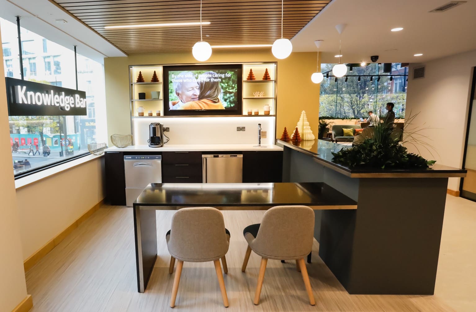 'Knowledge bar' area in the Lloyds Bank branch, with tea and coffee-making facilities, seating, an information screen and a large window with a view of Oxford Street.